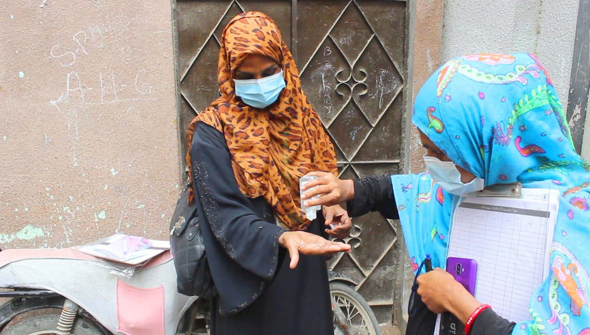 Vaccinator using hand sanitizer as a Covid precaution in a Polio immunization campaign in Pakistan